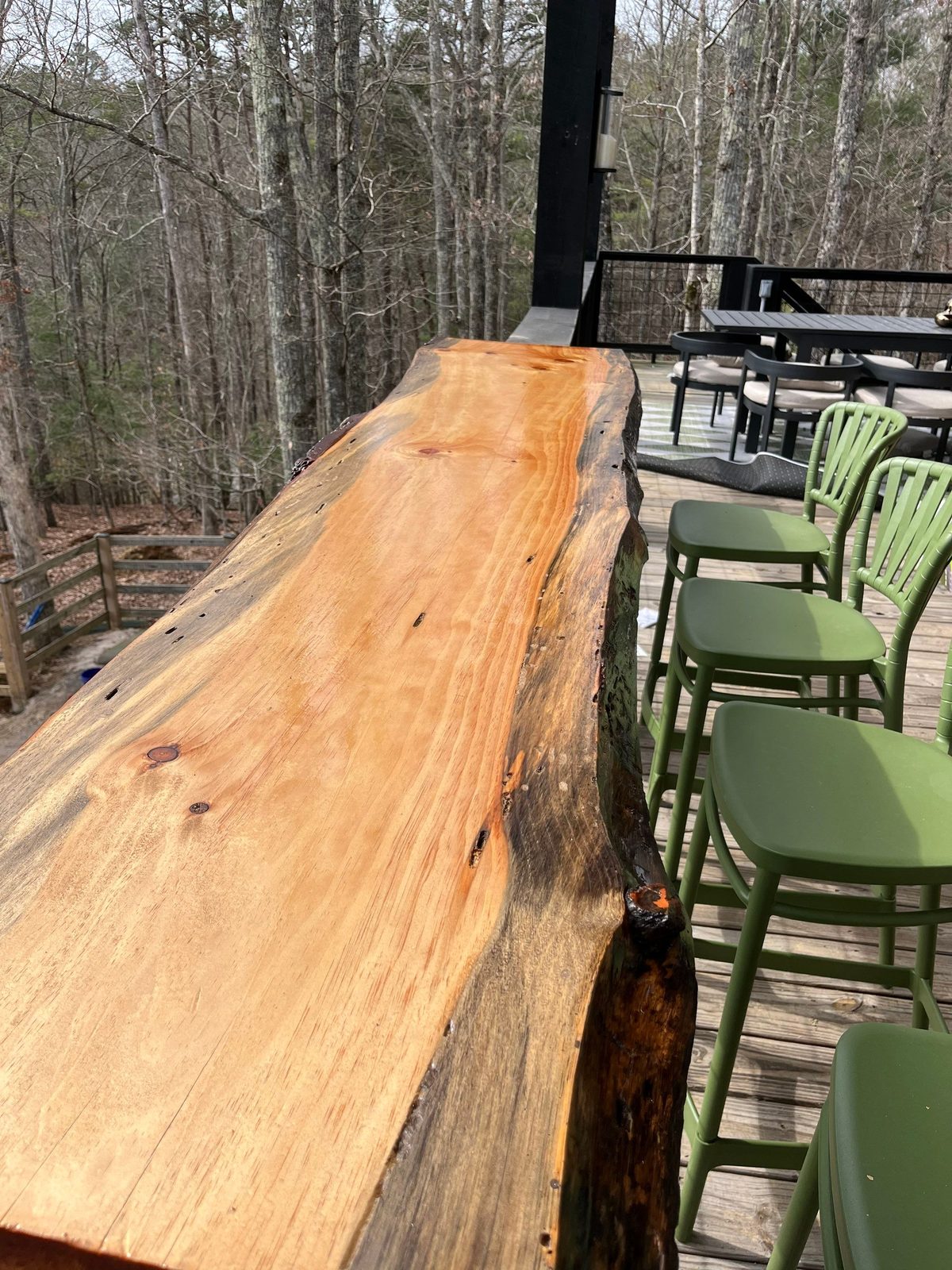 Live-edge wood bar top along a cabin deck railing with green stools