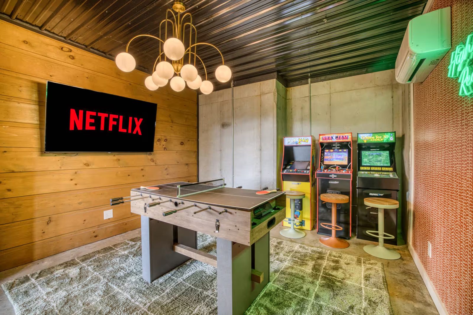 Arcade cabinets and games table in the converted Morganton cabin game room with wood feature wall